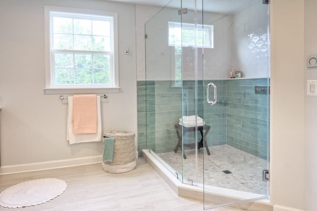 Spa-style primary bathroom remodel in Pewaukee WI with large-format porcelain tile, frameless glass walk-in shower, and freestanding soaker tub