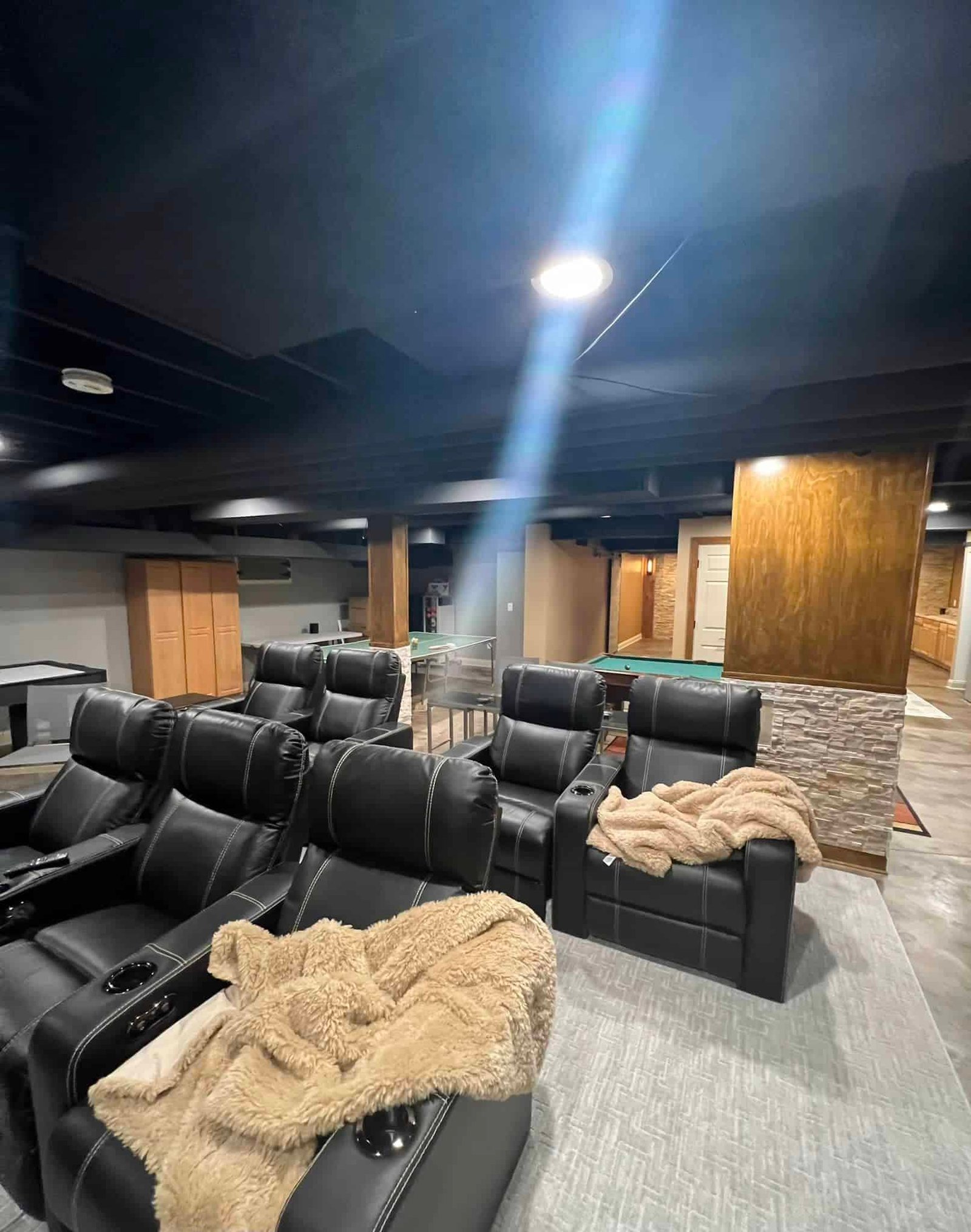 Fully finished Wisconsin basement featuring home theater recliners, pool table, ping pong table, and stone accent column with dark painted ceiling