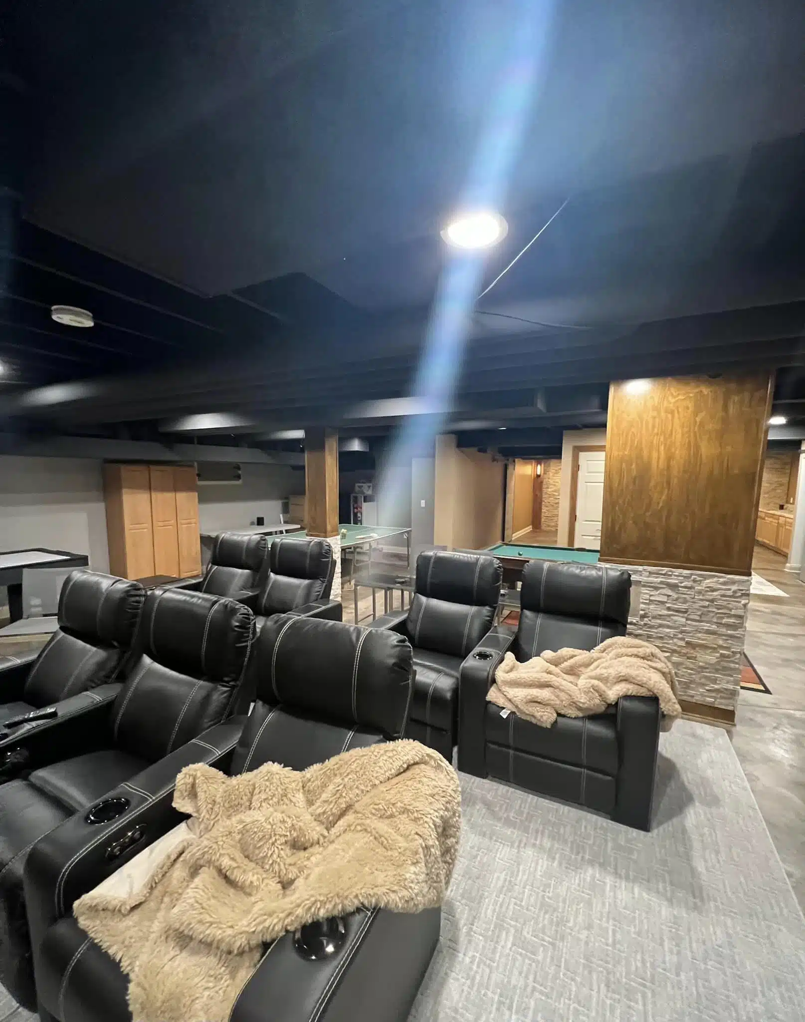 Fully finished Wisconsin basement featuring home theater recliners, pool table, ping pong table, and stone accent column with dark painted ceiling
