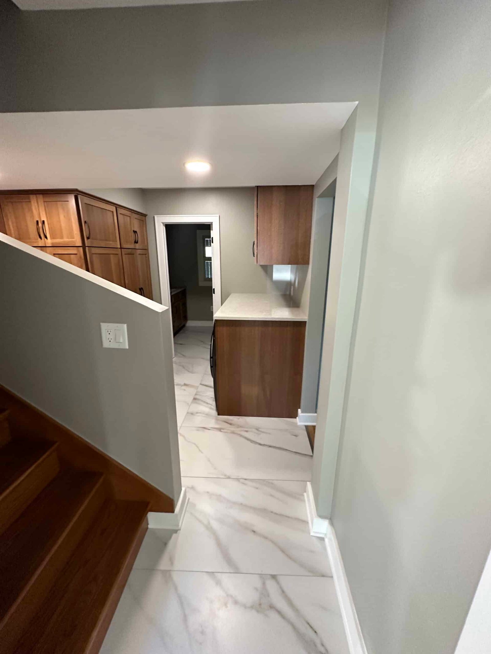 View from the staircase landing of a finished Wisconsin basement remodel featuring a wet bar with walnut cabinetry, quartz countertop, and large-format marble-l