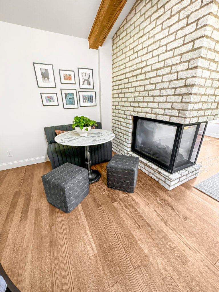 Finished lower level with a white painted brick fireplace, built-in banquette seating and wood-look flooring