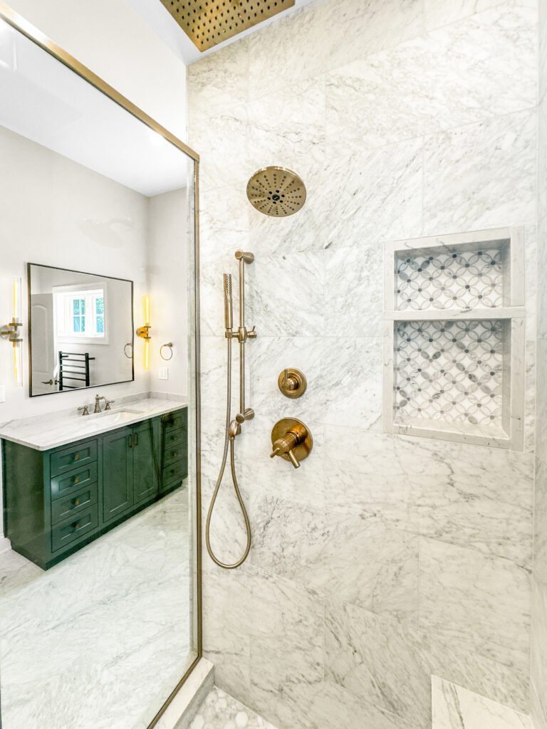 Bathroom remodel with a green vanity, brass fixtures and a marble tiled shower with niches