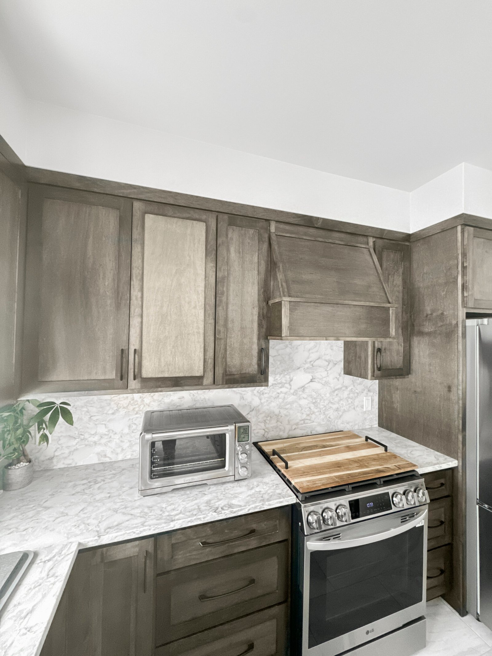 Remodeled Wisconsin kitchen featuring gray-stained wood cabinetry, marble-look quartz countertops and backsplash, custom wood range hood, and stainless steel LG