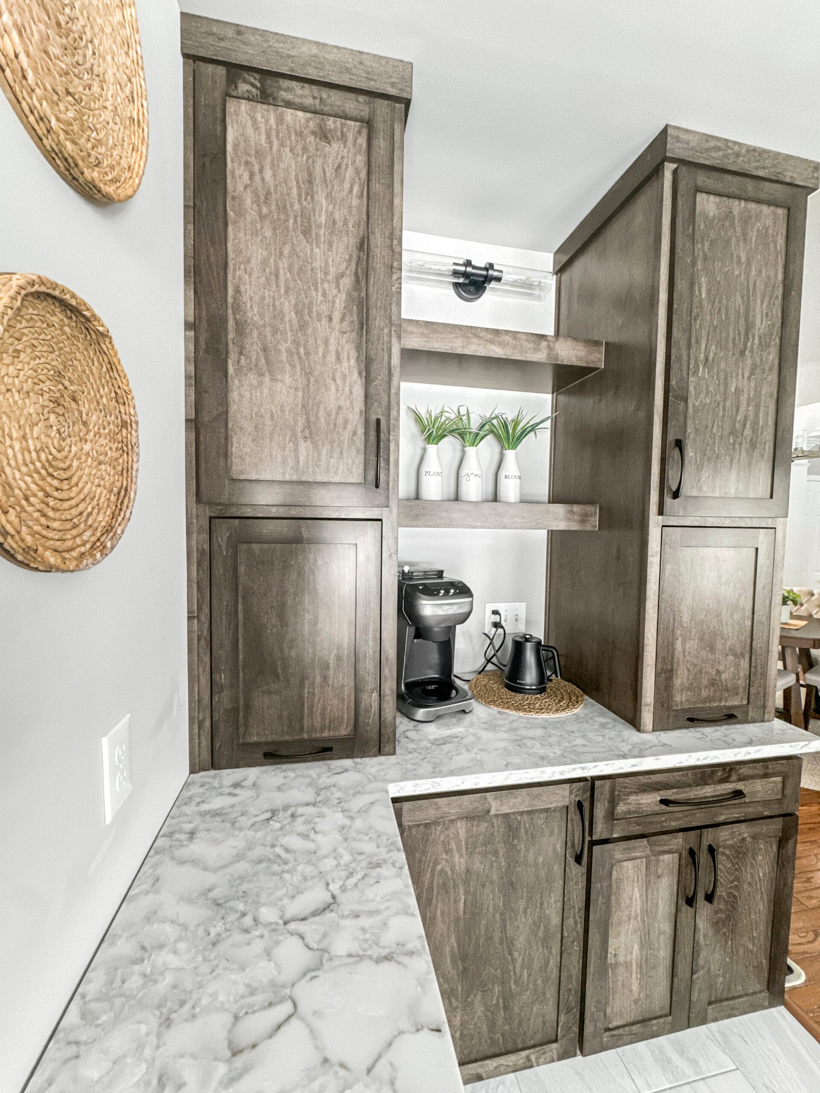 Remodeled kitchen with gray-toned wood cabinetry, marble-look quartz countertops, and a built-in coffee station with open shelving and decorative plants