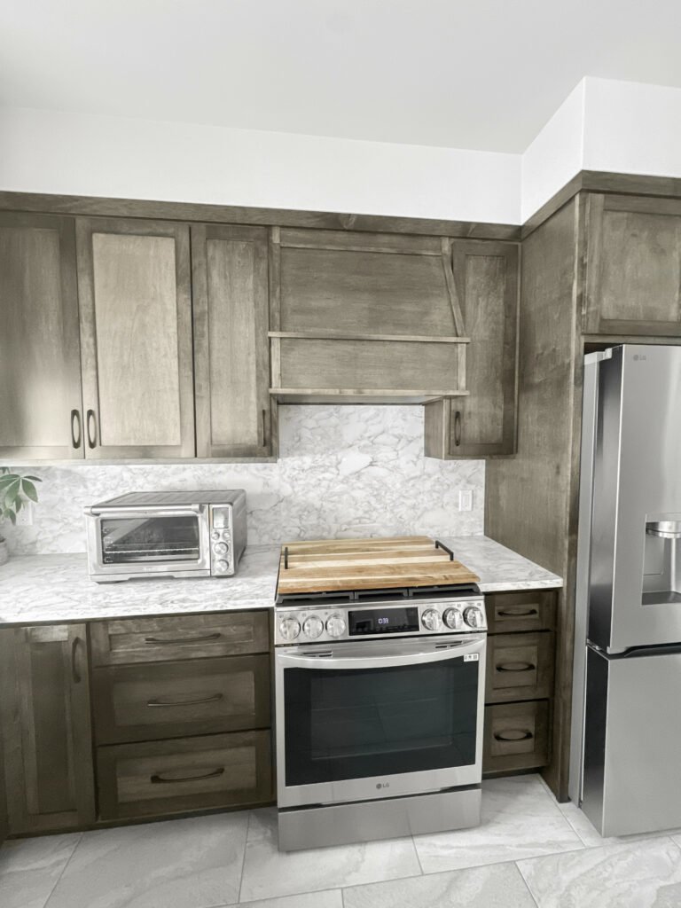 Kitchen with stained wood cabinets, a matching wood range hood and a marble-look backsplash