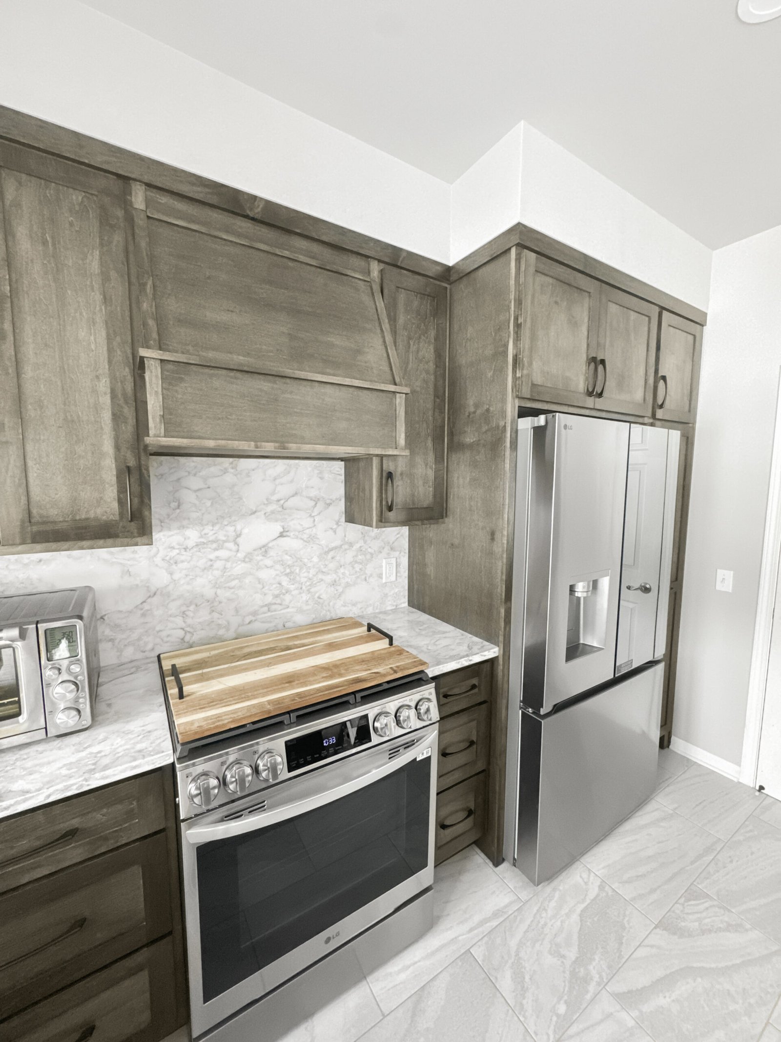 Stainless LG range and French-door refrigerator flanked by gray-stained cabinetry and marble-look tile flooring in a Wisconsin kitchen remodel