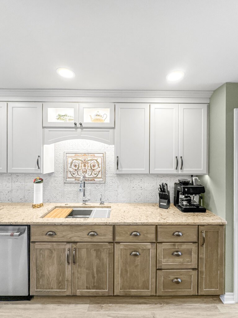 Kitchen with white shaker upper cabinets, stained lower cabinets and a tile medallion above the sink