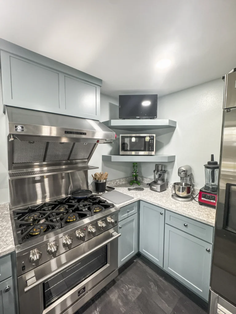 Kitchen range wall with a stainless hood, gas cooktop and open shelving beside the refrigerator