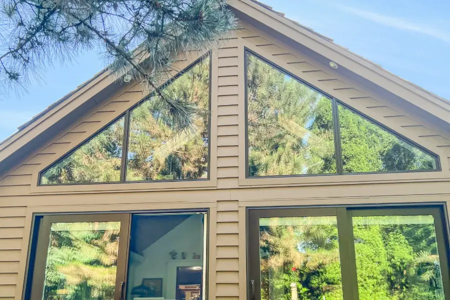 Close view of a sunroom addition gable with angled glass panels over sliding doors and new tan lap siding